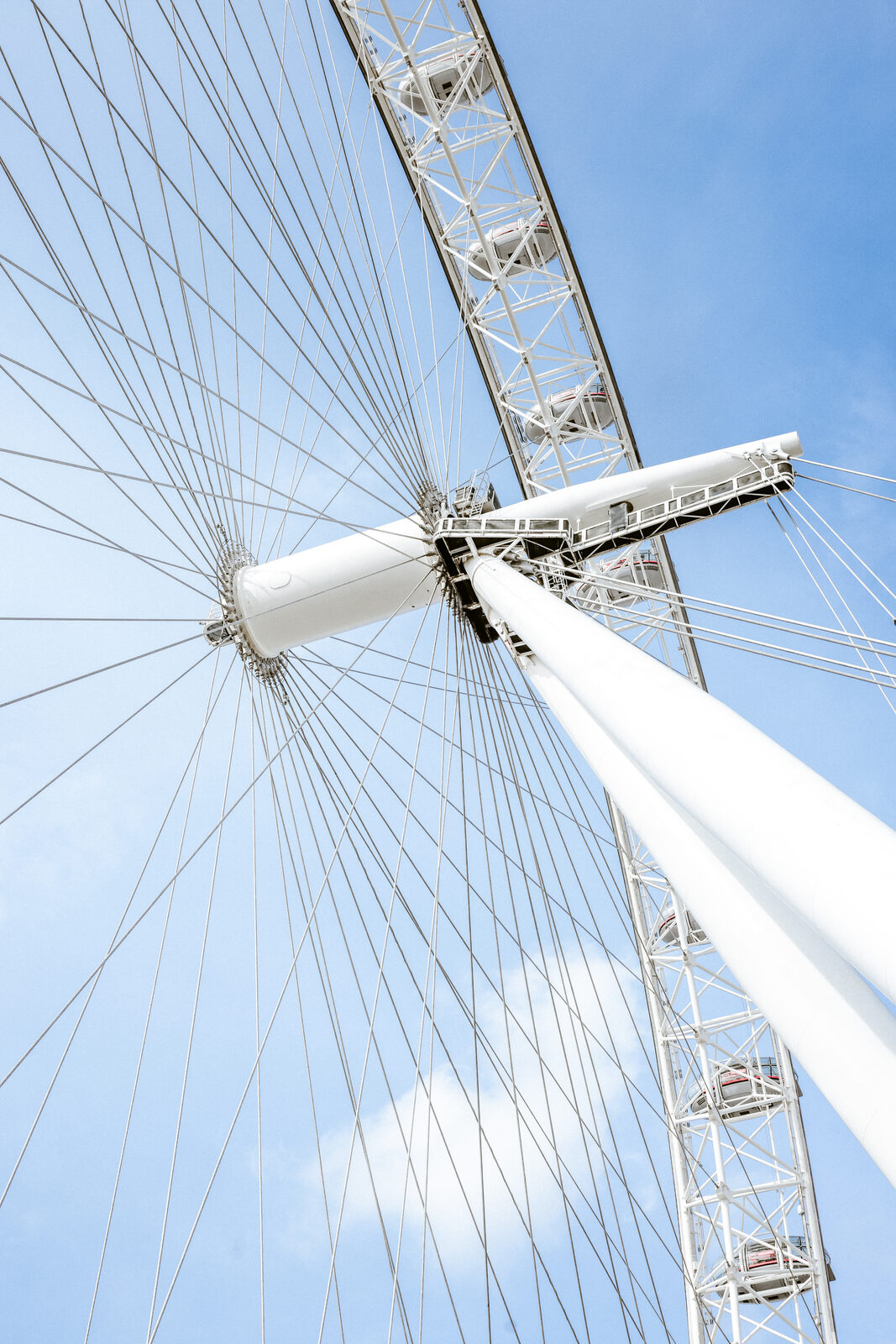 An upward, graphic view of the London Eye's spokes and support structure against a clear blue sky.